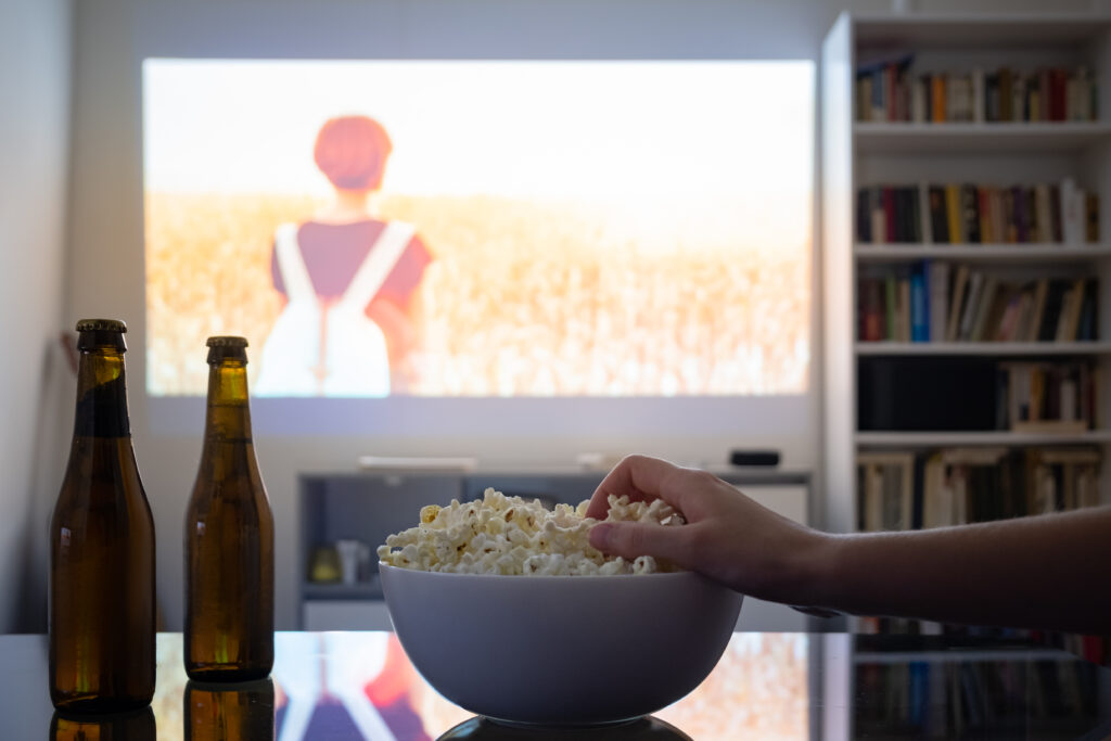 Picture of a projector with a hand grabbing popcorn from a bowl on a table