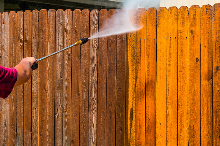 Picture of a person power washing a wooden fence 