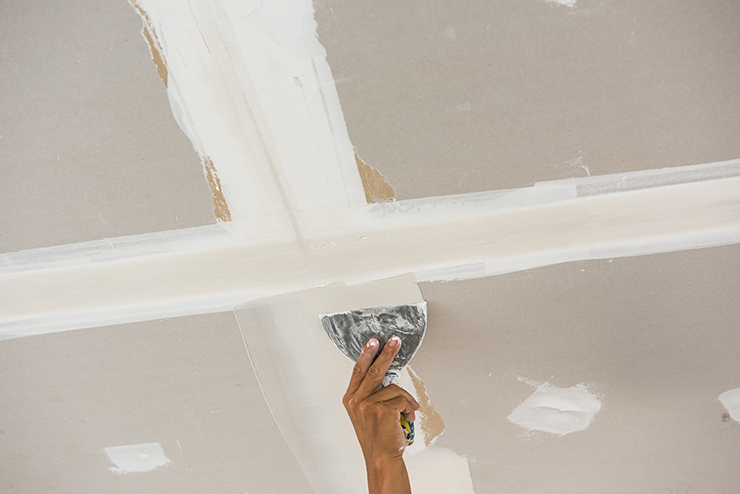 Picture of a hand holding plastering tools plastering a ceiling