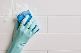 Closeup of a person wearing cleaning gloves scrubbing bathroom tile with a sponge