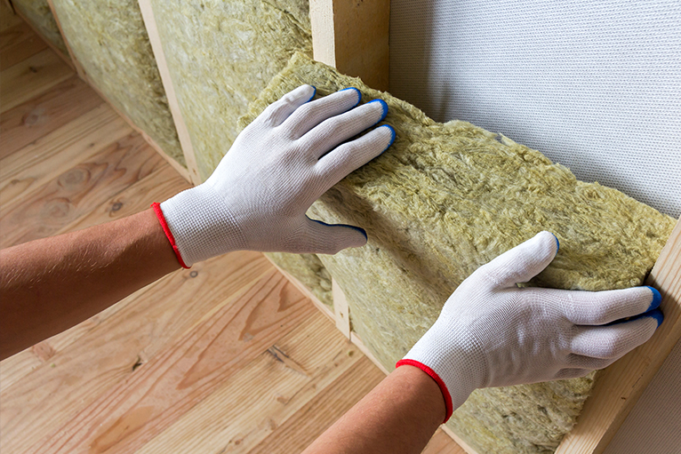 Close-up of worker hands in white gloves inserting rock wool insulation in wooden frame.