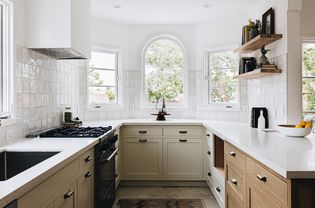 Cabinets painted tan in kitchen with white walls and wooden shelving
