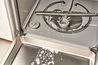 Open dishwasher with soapy water around drain and door