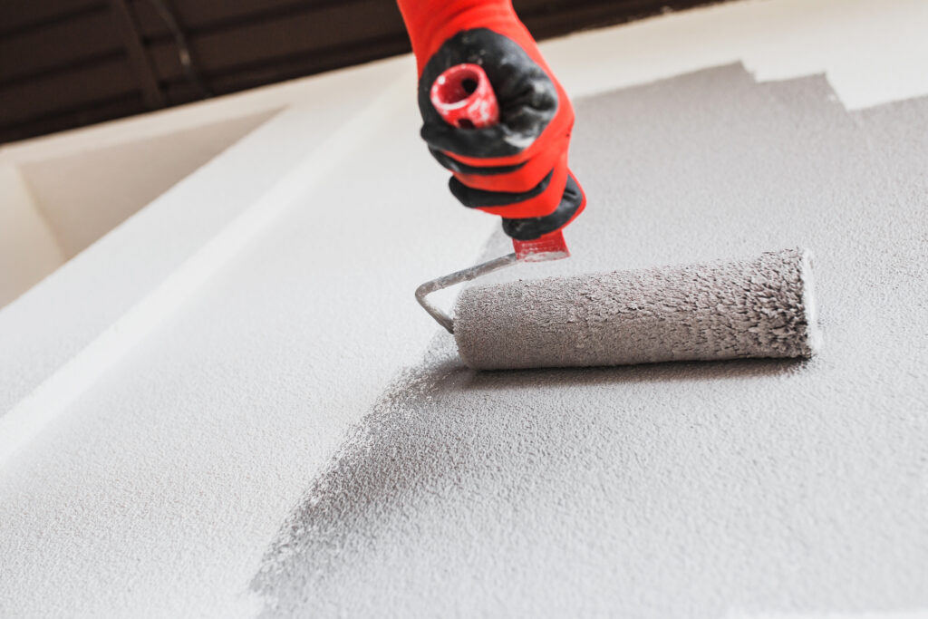 Picture of a roller with grey paint being applied to a wall