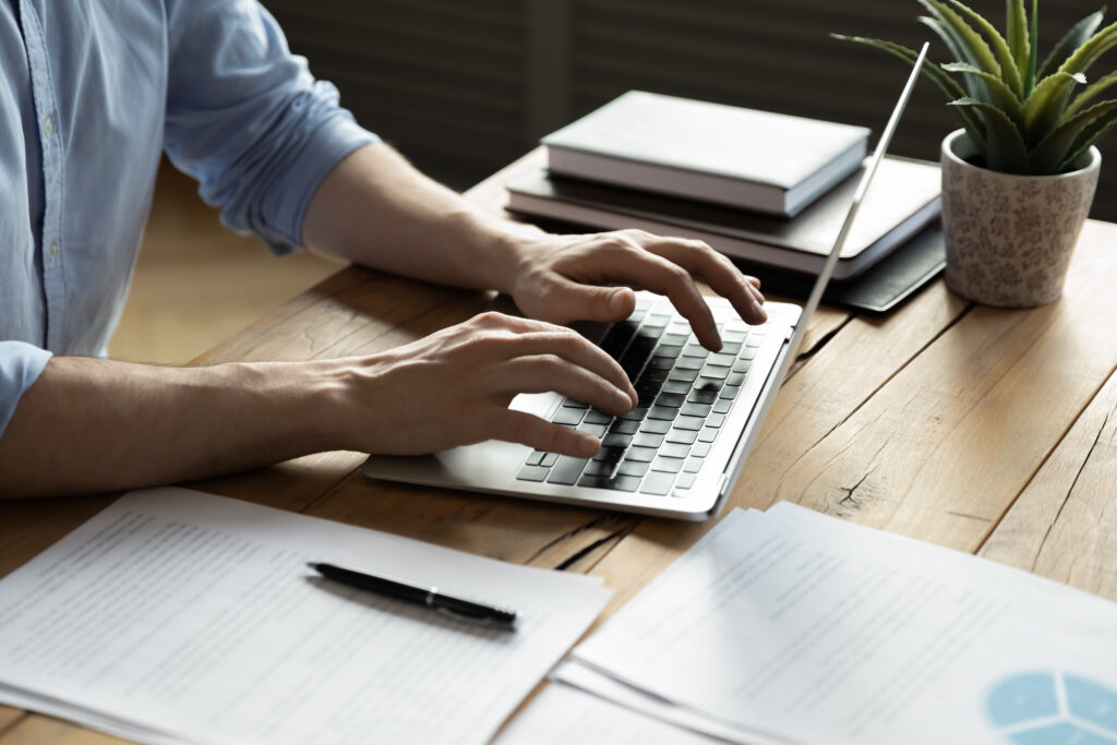 Picture of a person researching on laptop with paper and pen nearby