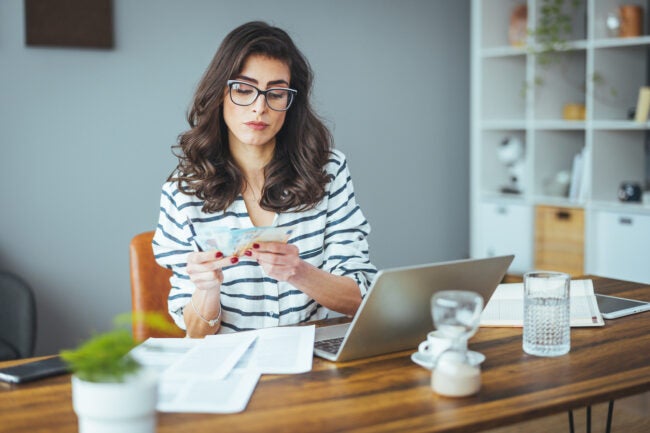 A woman looks at money while sitting in front of a computer.