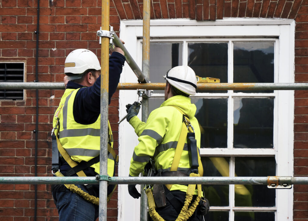 Picture of scaffolding with two tradespeople in white helmets building the scaffolding