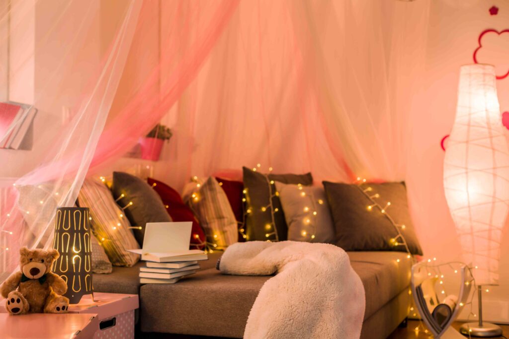 Picture of a sofa with drapery and fairy lights over the grey and red pillows 