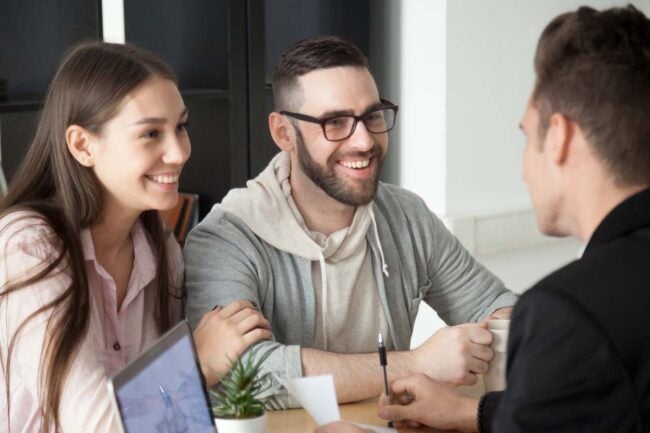 A man and a woman smile as they talk to a person with a computer.