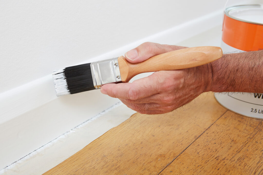 Picture of a man with a thin paintbrush painting the skirting board white